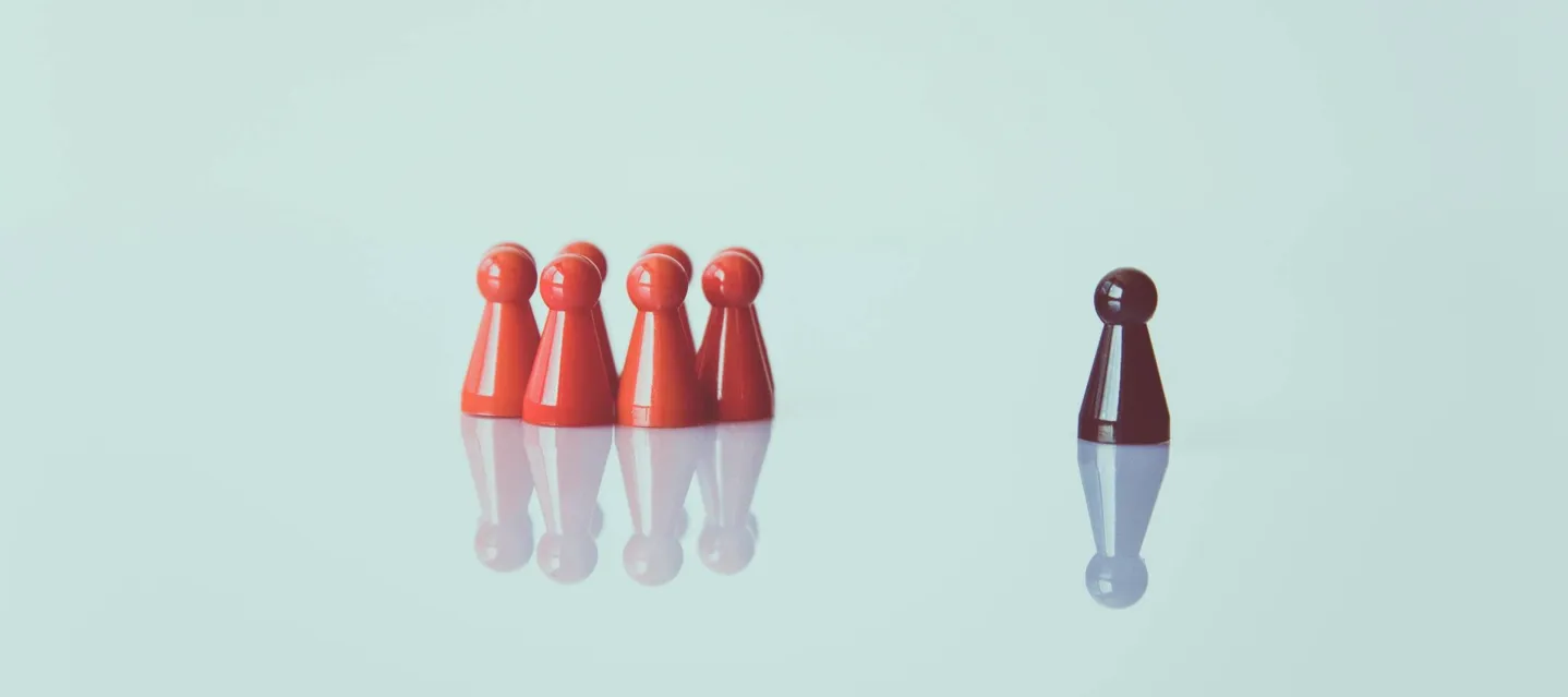 One dark game piece standing apart from a group of red game pieces.