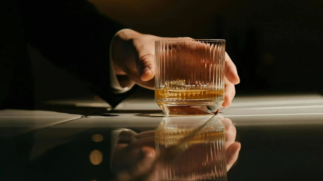 A person holding a glass of bourbon at a dark table